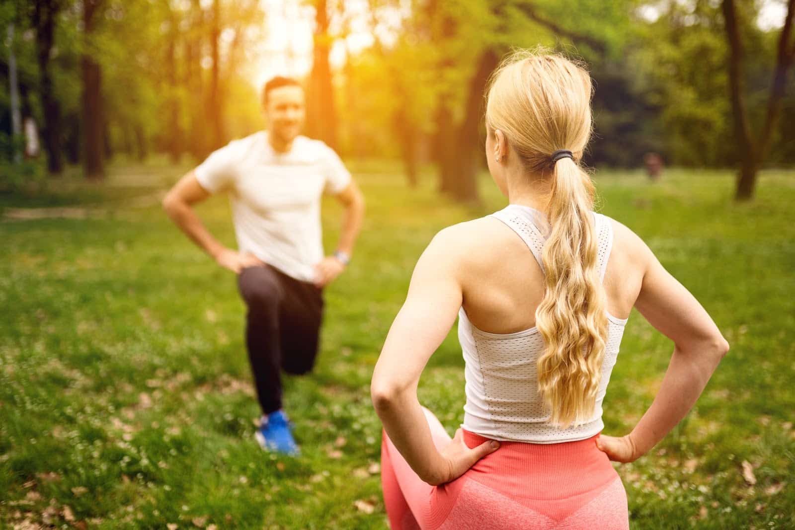 Fit young man and woman exercising in park. Smiling caucasian couple doing workouts on grass on sunny morning.